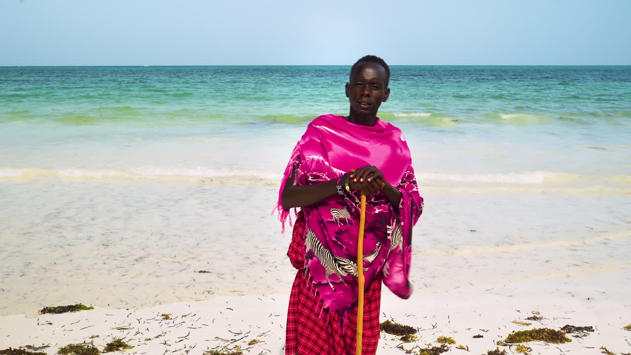 hombre africano nativo vestido de rosa sosteniendo palos en la playa de arena