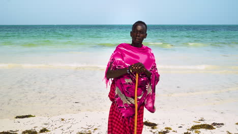 Hombre-Africano-Nativo-Vestido-De-Rosa-Con-Soportes-De-Palo-En-La-Playa-De-Arena