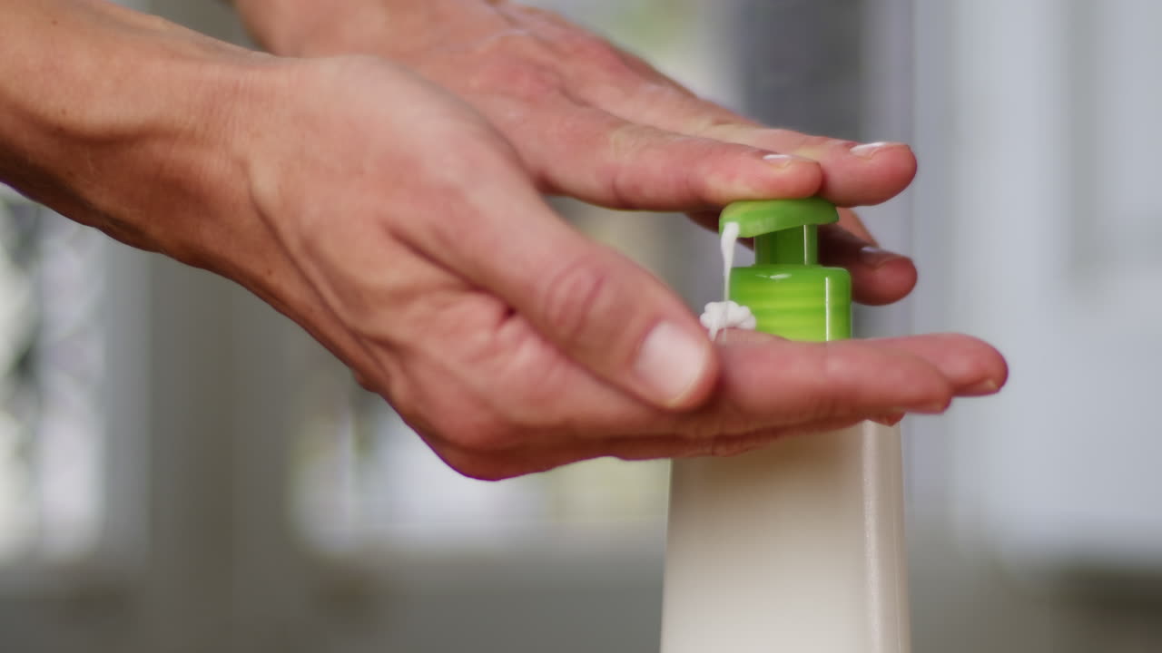 Young man squeezing a white moisturizer from a tube on his hand close-up. Morning routine. Beauty and care concept.