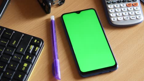 smartphone with green screen on a desk with office supplies