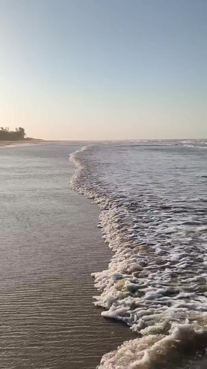Ondas Suaves Quebrando em uma Praia de Areia ao Pôr do Sol