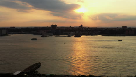 Aerial-footage-of-the-Hudson-River-in-New-York-as-the-drone-rises---focuses-on-the-sunset-while-two-boats-go-by-in-opposite-directions-with-a-sailboat-in-the-middle