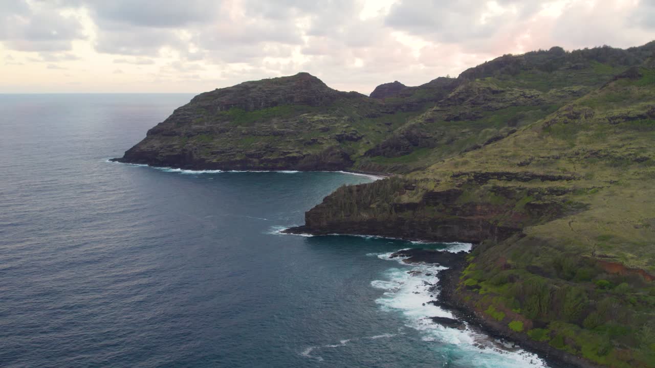 Riprese aeree 4K con drone di onde oceaniche blu che si infrangono sull'alta scogliera di una montagna rocciosa.