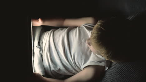 niño usando una tableta viendo una película cubierta por la sábana en la noche 1