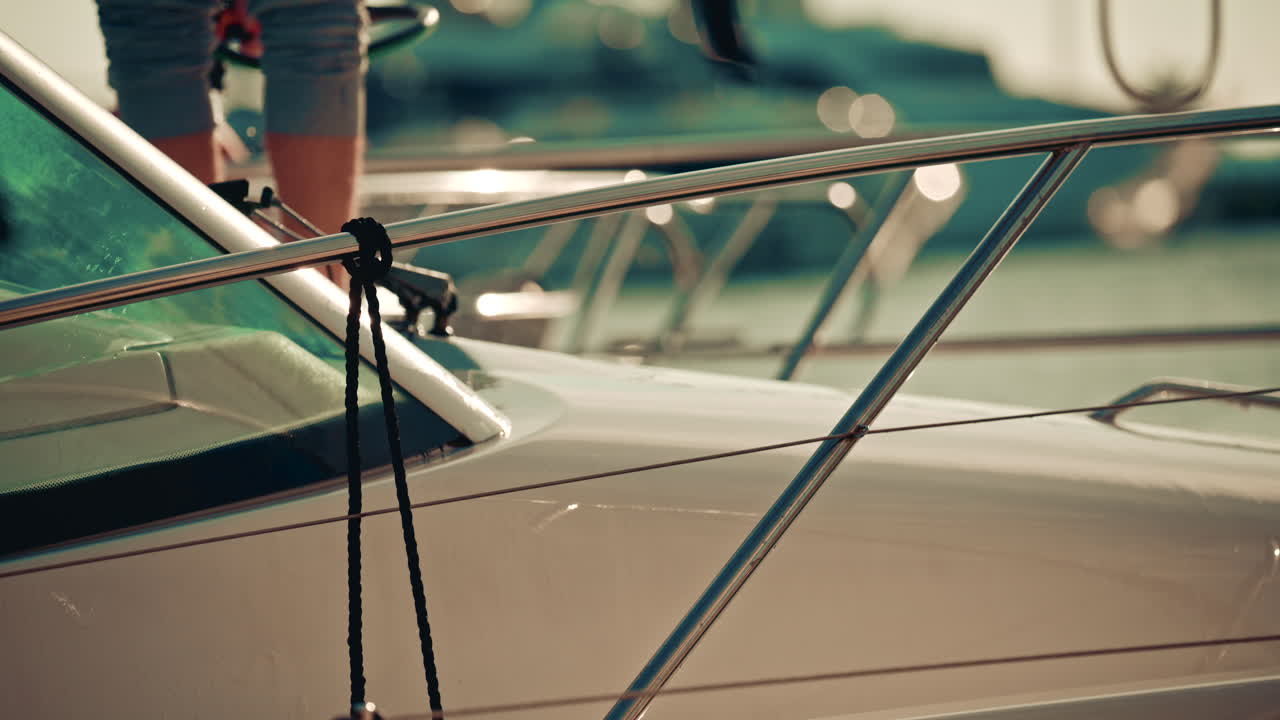 Hands washing a yacht's deck with a hose, with water spraying in the air and sunlight creating sparkling highlights on the boat's railings
