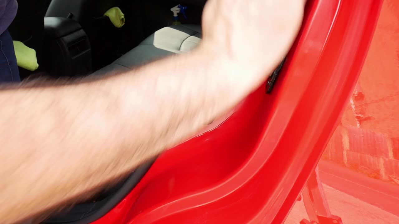 Close up hand polishing a door shut jamb on a red car with white microfibre pad