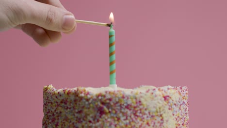 foto de estudio de un pastel de cumpleaños giratorio cubierto con decoraciones y una sola vela encendida y apagada