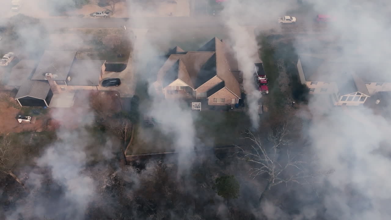 Close up aerial footage that is panning across houses that are covered in smoke from a wildfire that is very close to the neighborhood.
