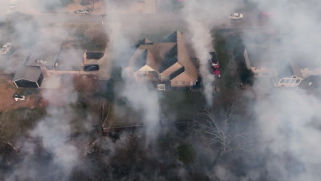 close up aerial footage that is panning across houses that are covered in smoke from a wildfire that is very close to the neighborhood.