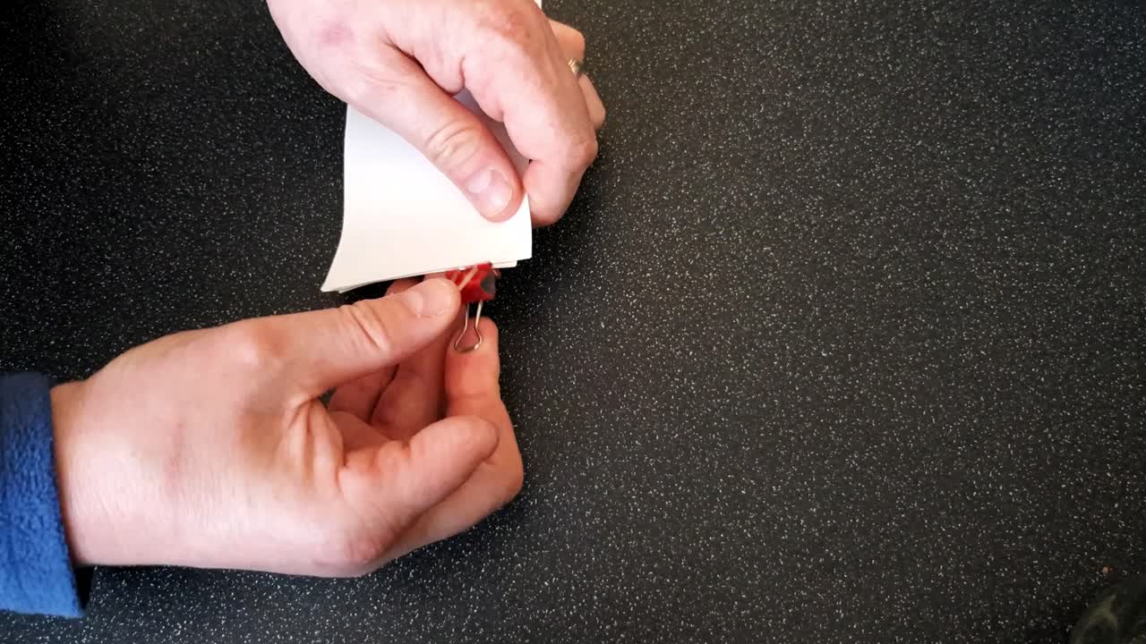 Male with a partially amputated index finger on his right hand putting a red bull dog clip on some white strips of paper