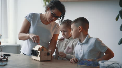 woman helps little boy and girl interested in science and technology to build a robot