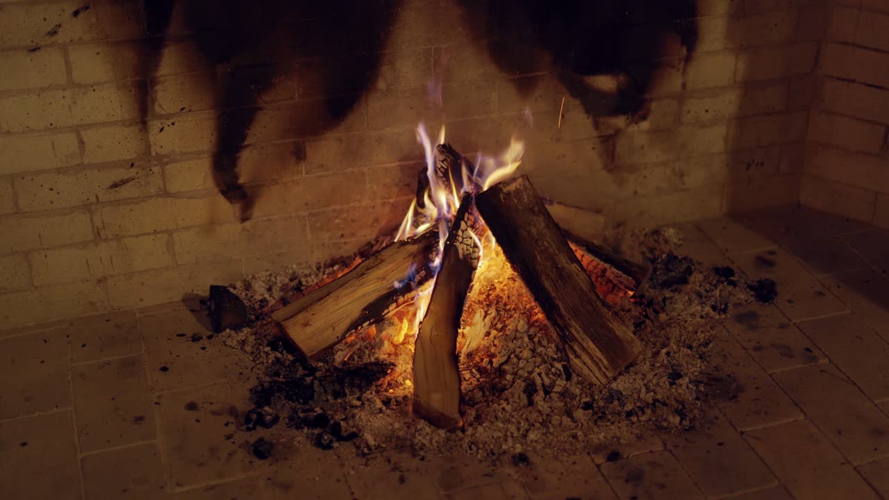 Woods burning in fireplace indoors. Sparks of bright fire woods on bricks wall background. Romantic and holiday atmosphere. Close-up.