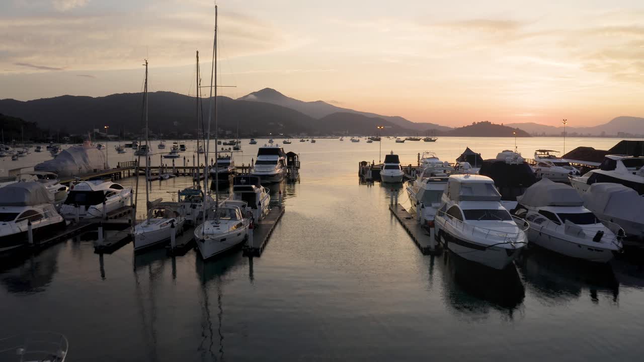 Drone che vola tra yacht, barche e barche a vela ormeggiati in un porto turistico con un bellissimo tramonto