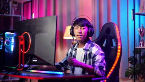 asian teen boy gamer smiling to camera and showing thumb up while playing video game on computer