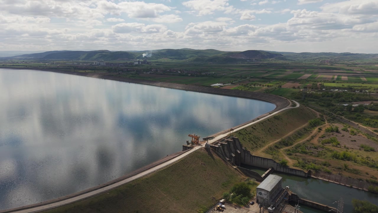 Luftfoto af en stor dæmning, der holder et roligt reservoir, omgivet af grønt landskab.