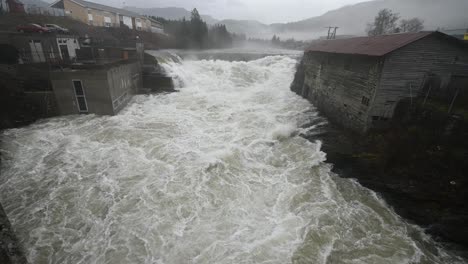 handheld static shot of a powerful flooded river rushing under a bridge in voss, norway. slow motion reveals the intense flow and energy of the water