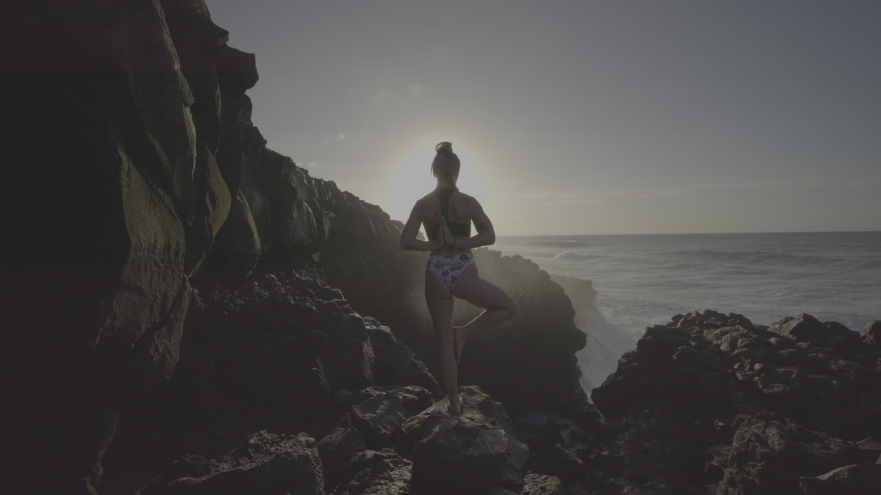 Donna che pratica yoga su una costa rocciosa all'alba