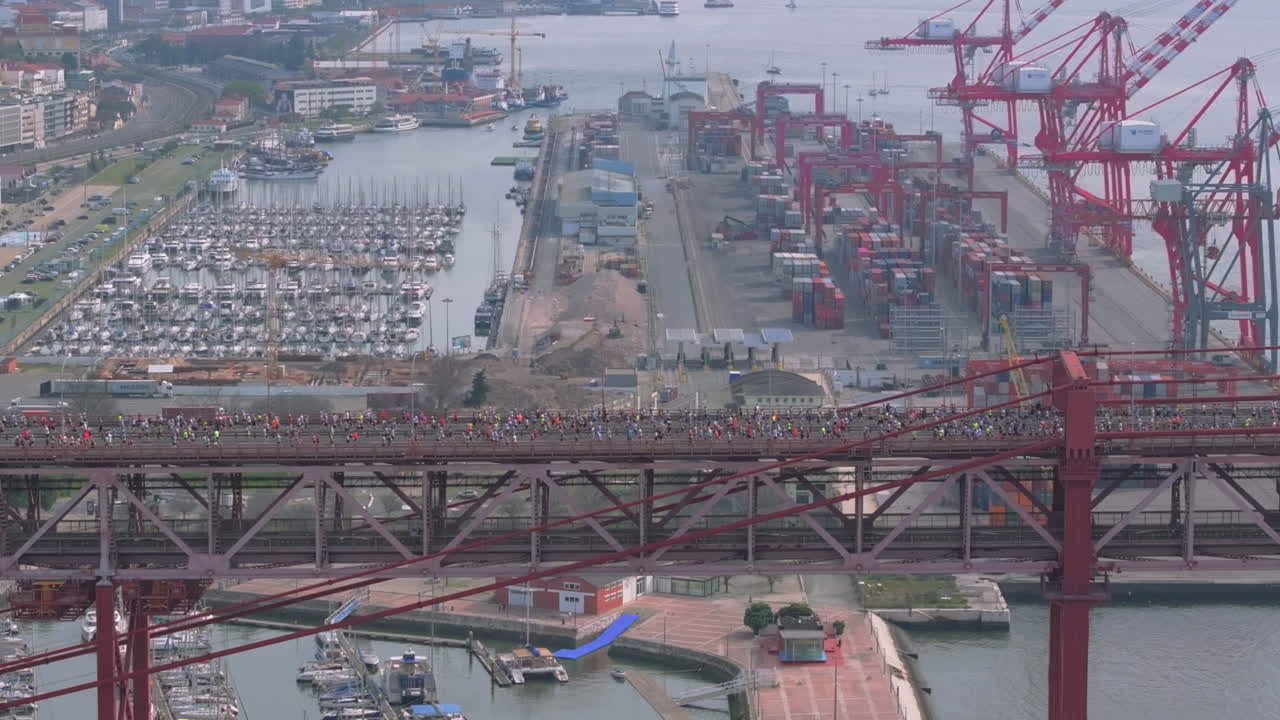 Side-on aerial drone shot of half marathon and 10K long-distance running event in Lisbon, Portugal, Europe. Runners crossing the iconic famous red 25th April bridge, neutral grading
