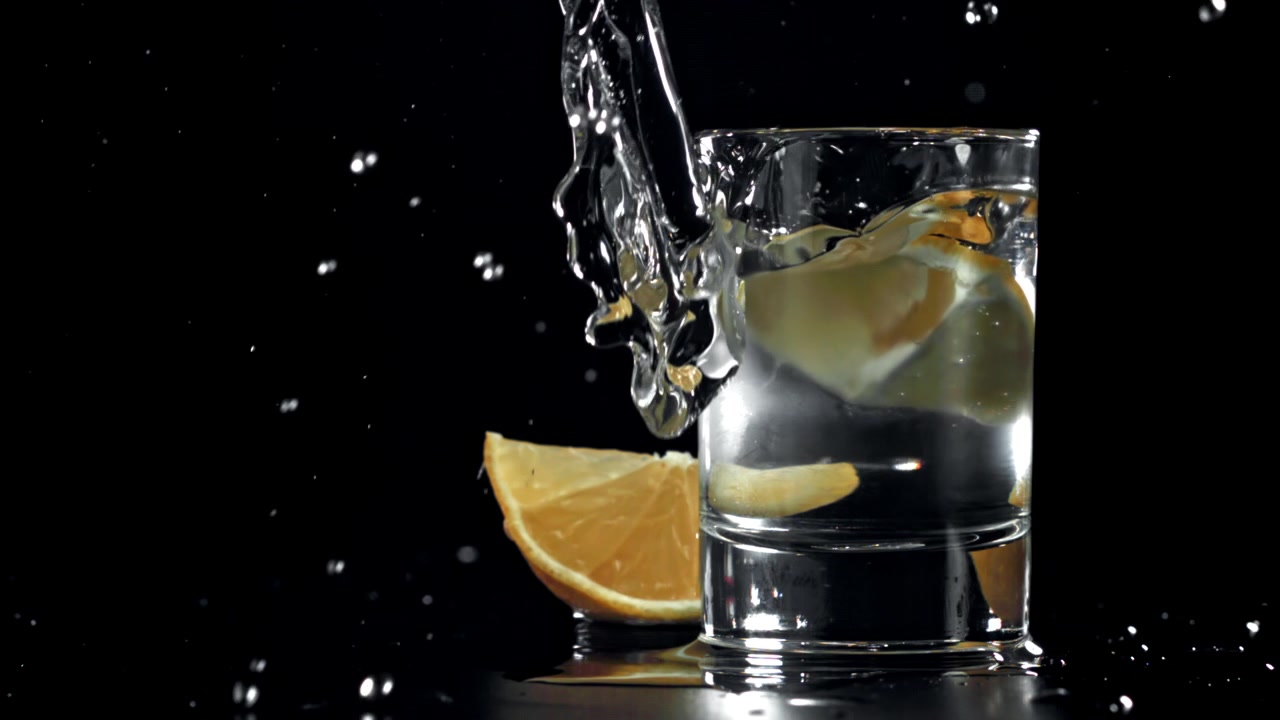Movimento rallentato: fetta di limone che cade in un bicchiere d'acqua con schizzi