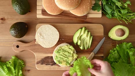 crop woman adding lettuce on hamburger bun