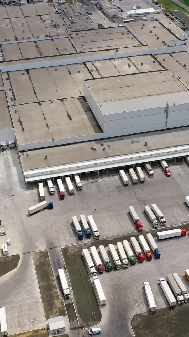 Modern industrial area with large trucks outdoors. Aerial view of huge manufacturing complex in summer. Camera moves up. Slow motion. Vertical video