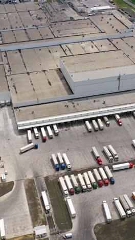 Modern industrial area with large trucks outdoors. Aerial view of huge manufacturing complex in summer. Camera moves up. Slow motion. Vertical video