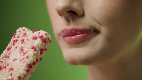 una foto ravvicinata di una giovane donna che si gode un delizioso gelato vegano con sapore di vaniglia e fragola di fronte allo sfondo verde a rallentatore