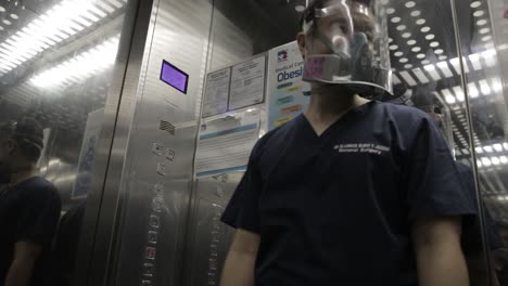 médico con respirador y protector facial, presionando el botón en el ascensor del hospital