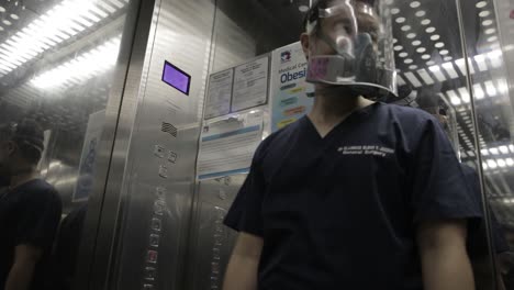 doctor wearing respirator and face shield, pushing button in hospital elevator