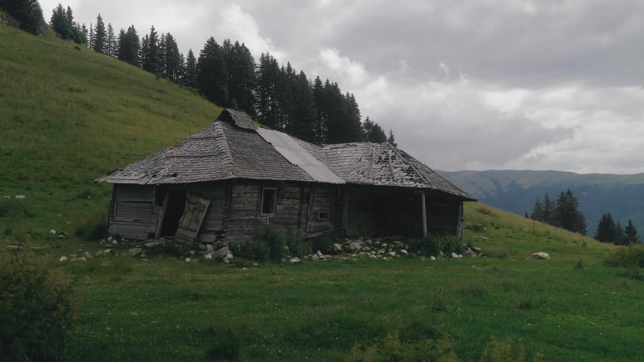 una toma panorámica izquierda revela una vieja cabaña de madera abandonada ubicada en un prado alpino de hierba verde