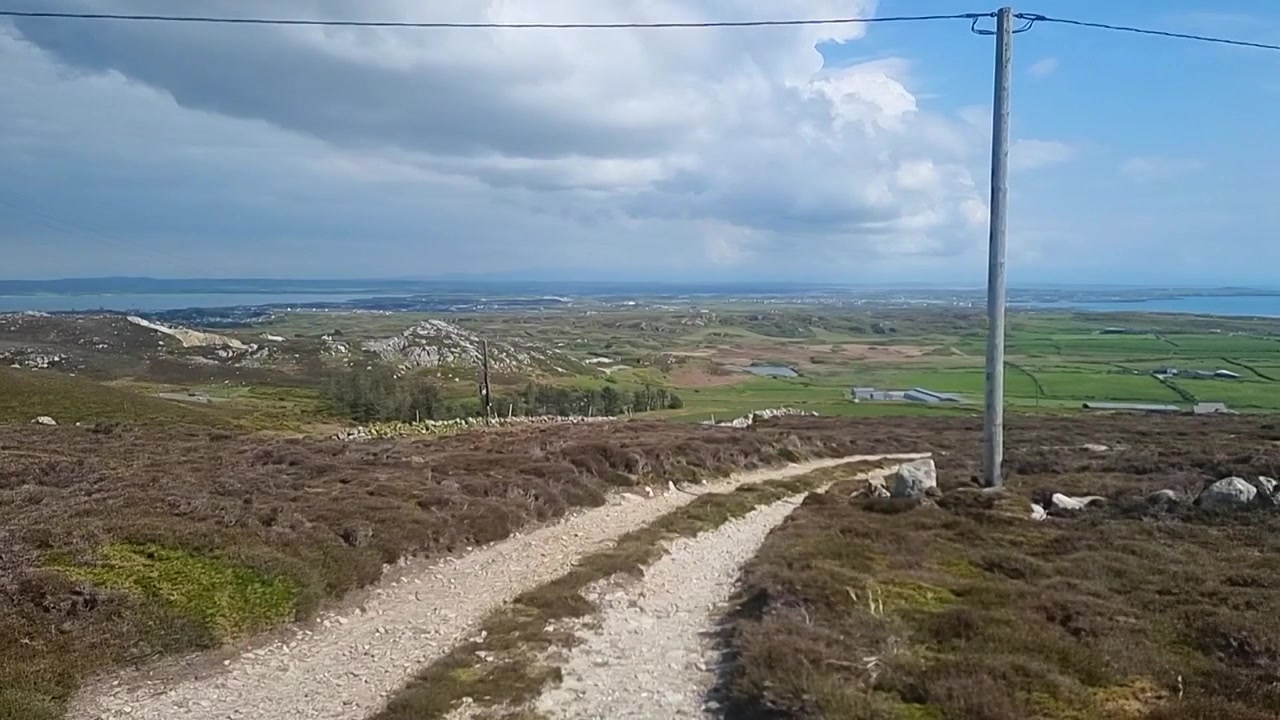 Panoramatický pohled z drsného vrcholu hory Holyhead přes slunnou venkovskou vřesovištní turistickou stezku.