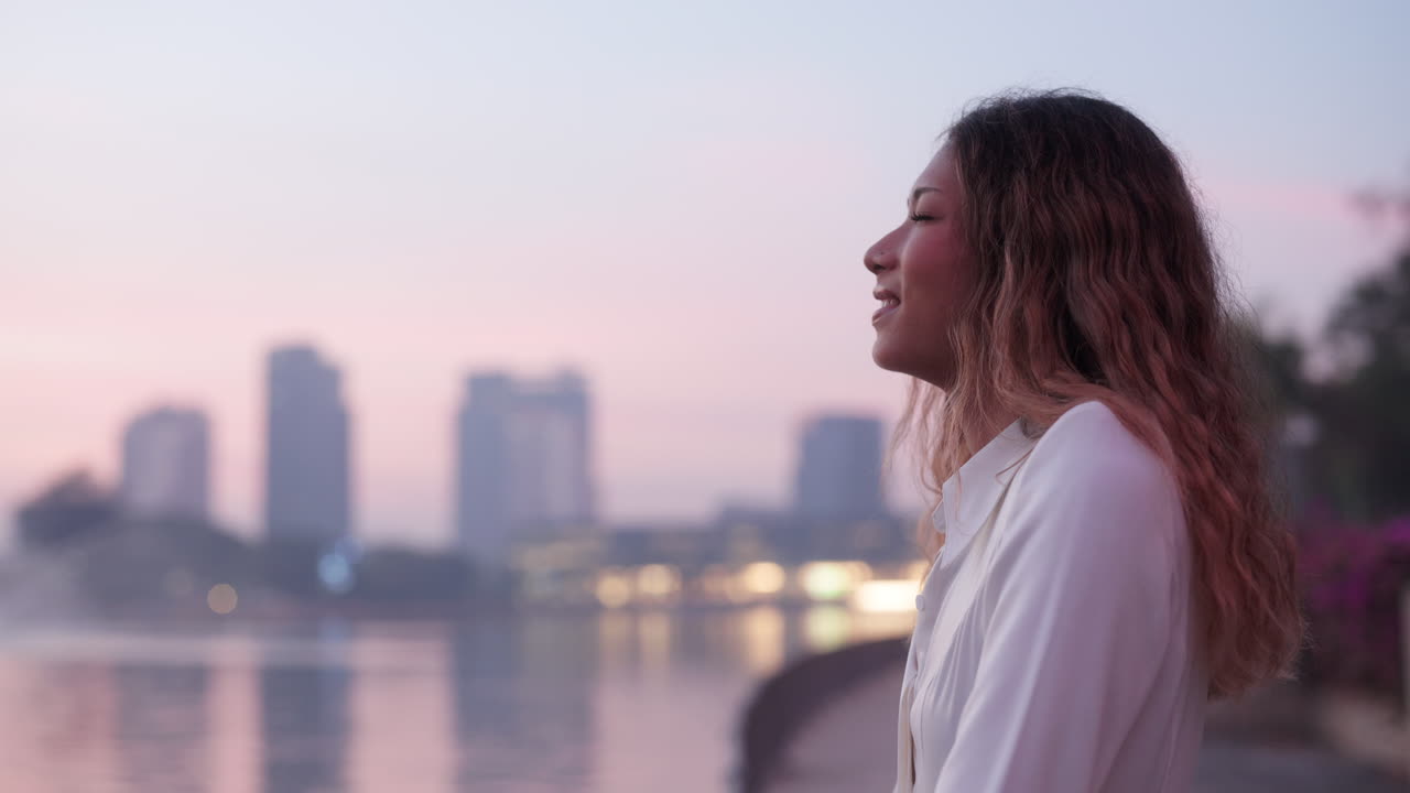 Young Woman Smiling by a Lake with Cityscape at Dusk