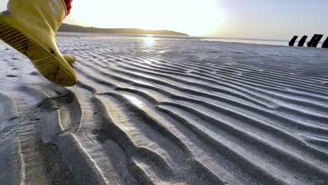 Walking-in-yellow-rubber-boots-on-a-sandy-beach-at-sunrise