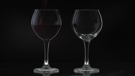 two wine glasses, one full and one empty, on a black background