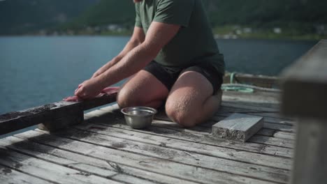 campista cortando carne fresca para cocinar en una plataforma de madera junto a la orilla del lago