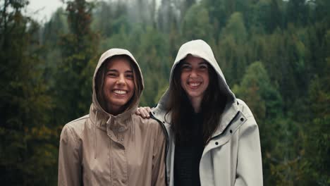 Zwei-Mädchen-In-Leichten-Jacken-Mit-Kapuze-Freuen-Sich-über-Den-Kommenden-Regen-Und-Schauen-In-Einem-Bergwald-In-Die-Kamera