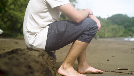 male-sitting-on-a-wooden-trunk-in-a-lonely-beach-of-Costa-Rica-Central-America-carribean-sea-ocean