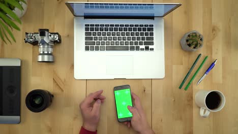 colocación plana de las manos del hombre usando el teléfono con pantalla verde en el lugar de trabajo