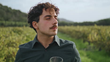 Young-winemaker-standing-vineyard-enjoying-smell-exquisite-white-wine-close-up.