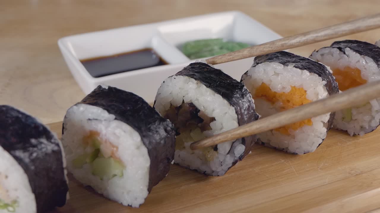tiro deslizante en cámara lenta de tomar un trozo de sushi de una tabla de servir de madera con palillos