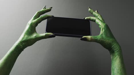 Video-of-halloween-green-monster-hands-holding-smartphone-with-copy-space-on-grey-background