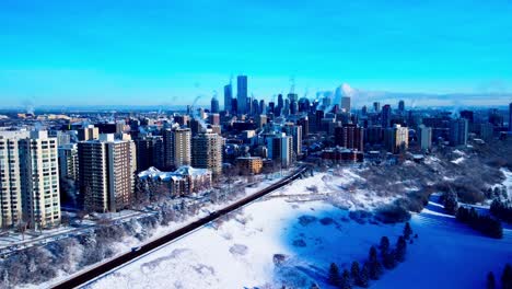 Winterluftdrohne-Hält-über-Schneebedeckten-Bäumen-Und-Dem-Talrand-Des-Nordwestblicks-Auf-Die-Innenstadt-Von-Edmonton,-Alberta,-Mit-Den-Höchsten-Gebäuden,-Die-über-Den-Blauen,-Klaren-Horizont-Hinausragen