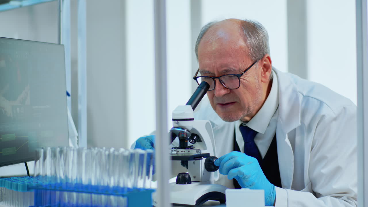 Laboratory scientist conducting experiment looking at microscope in busy lab