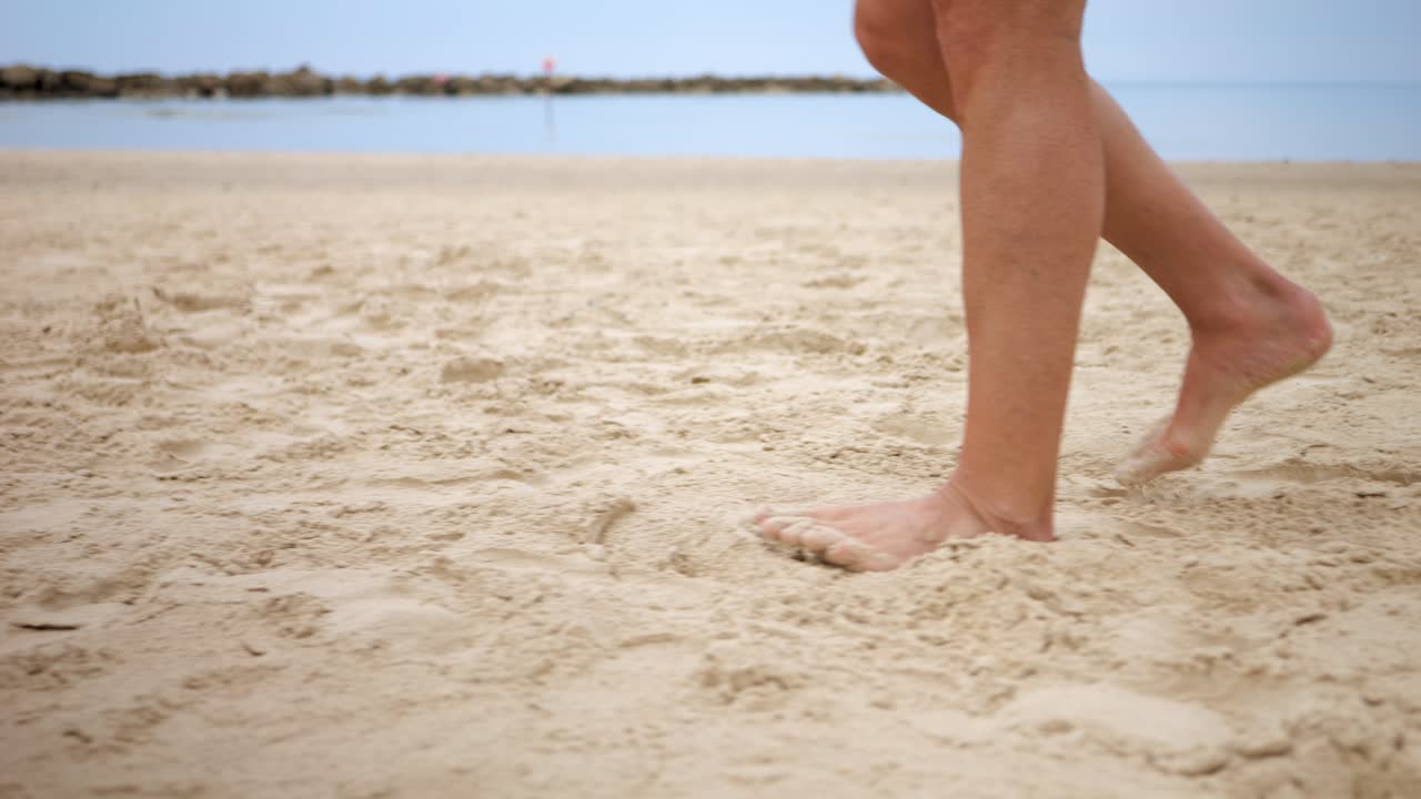 Sabbia che ammortizza una persona a piedi nudi che cammina lungo la spiaggia mantenendosi attiva