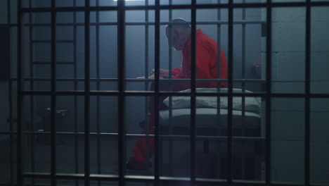 criminal sits on the bed in prison cell looks at barred window          (stock footage)