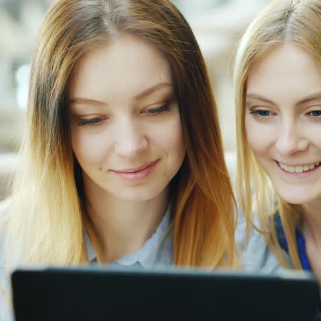 Two-Friends-Relax-In-A-Cafe-Looking-At-The-Tablet-Screen-1