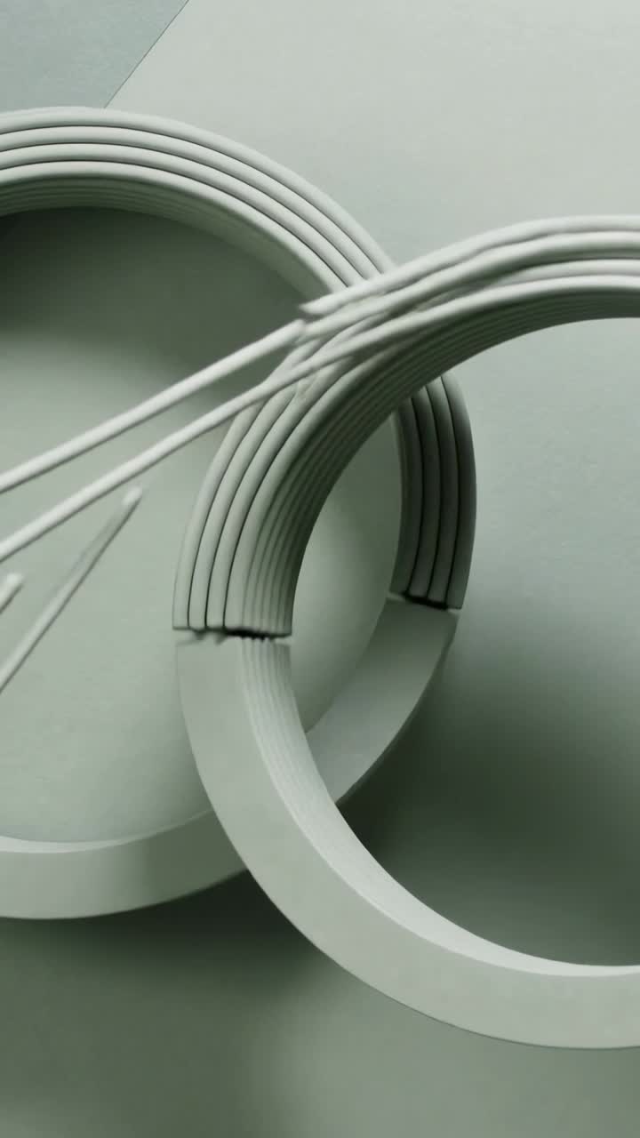 Video verticale: Fascio di aste che scorre e si inserisce in una fessura, infilando due anelli su una superficie opaca, formando un intreccio.