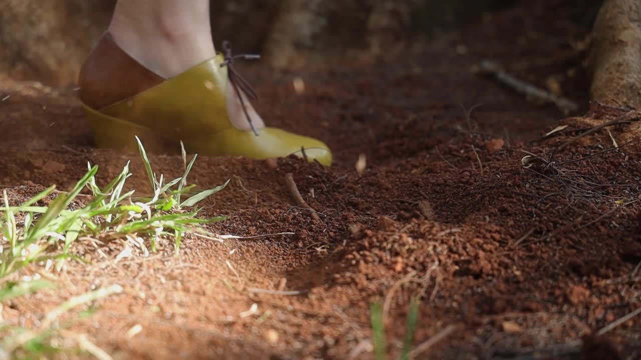 A woman wearing a yellow shoe splashing soil with her pams, White woman wearing yellow and brown fashionable shoes