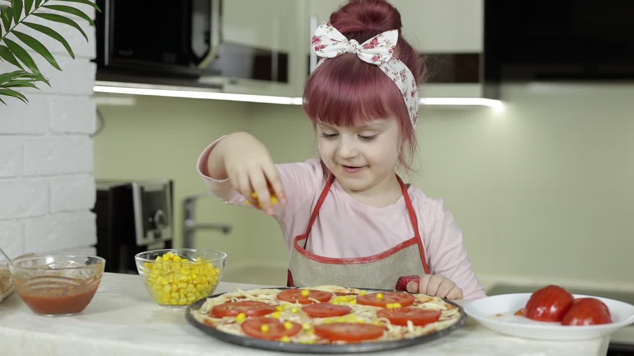 cocinando pizza. niño pequeño en delantal añadiendo maíz enlatado a la masa en la cocina