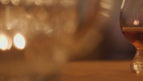 a row of whisky glasses sits on a wooden table in soft, warm candlelight. the background is blurred, creating a cozy, intimate mood